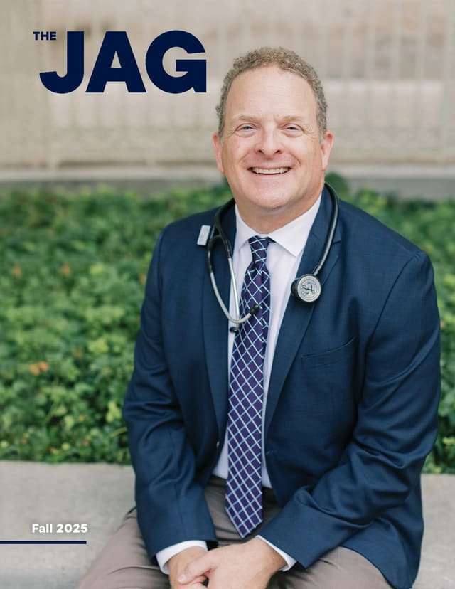 A smiling man in a blazer with a stethoscope poses for a photo